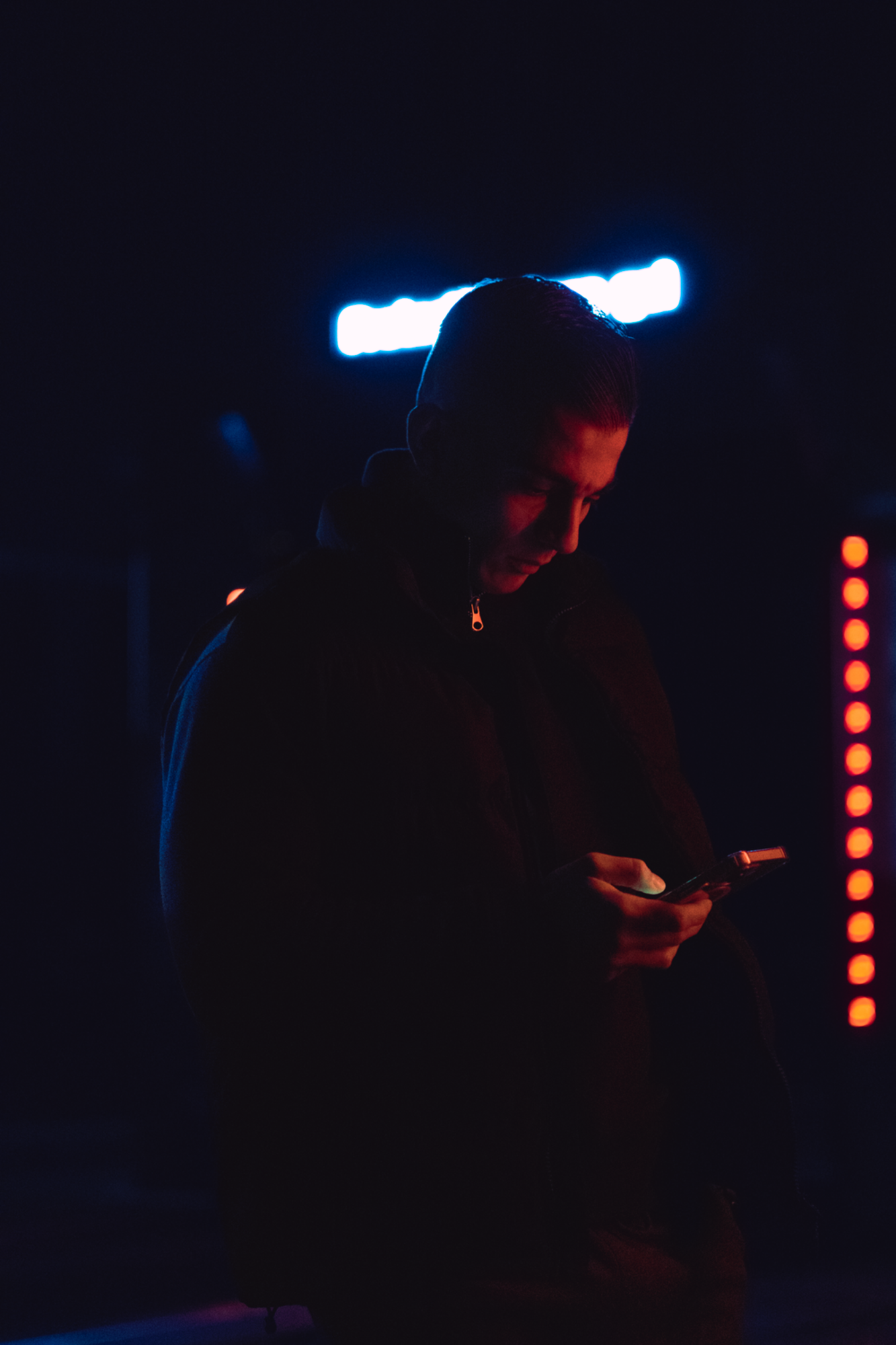Jeune homme de nuit sur son téléphone devant des lumières  – photographie Night shoot par luminéo