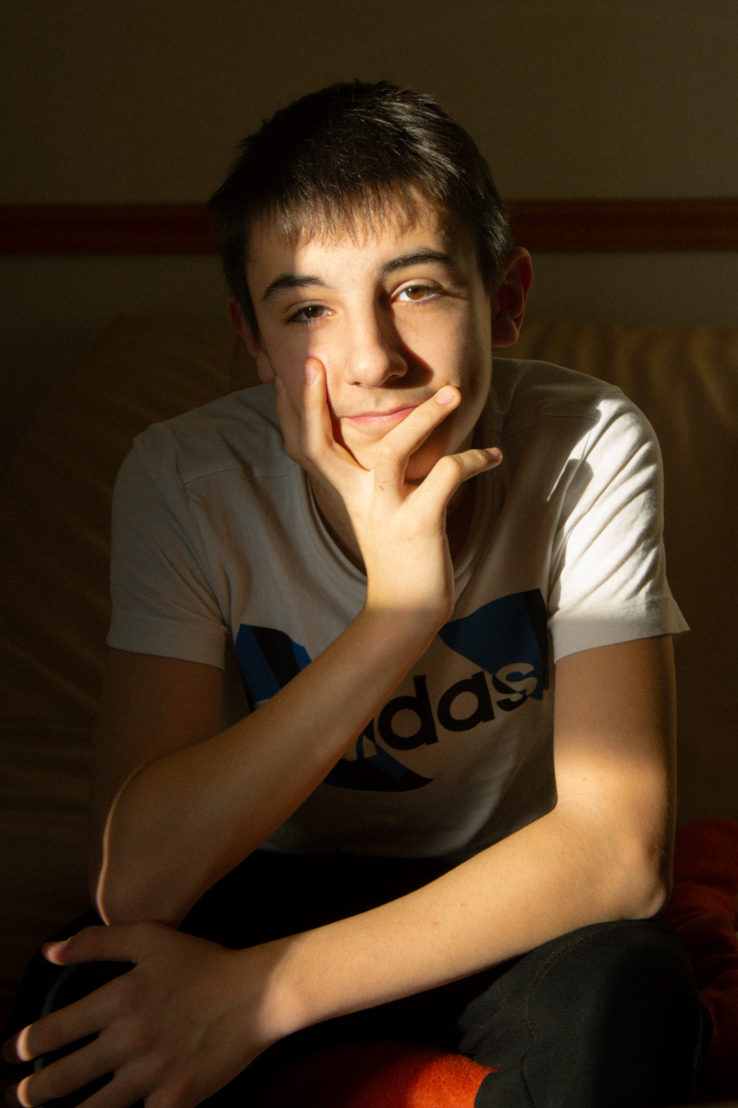 Jeune garçon posé et souriant dans un rayon de soleil à l’intérieur – portrait naturel par Luminéo