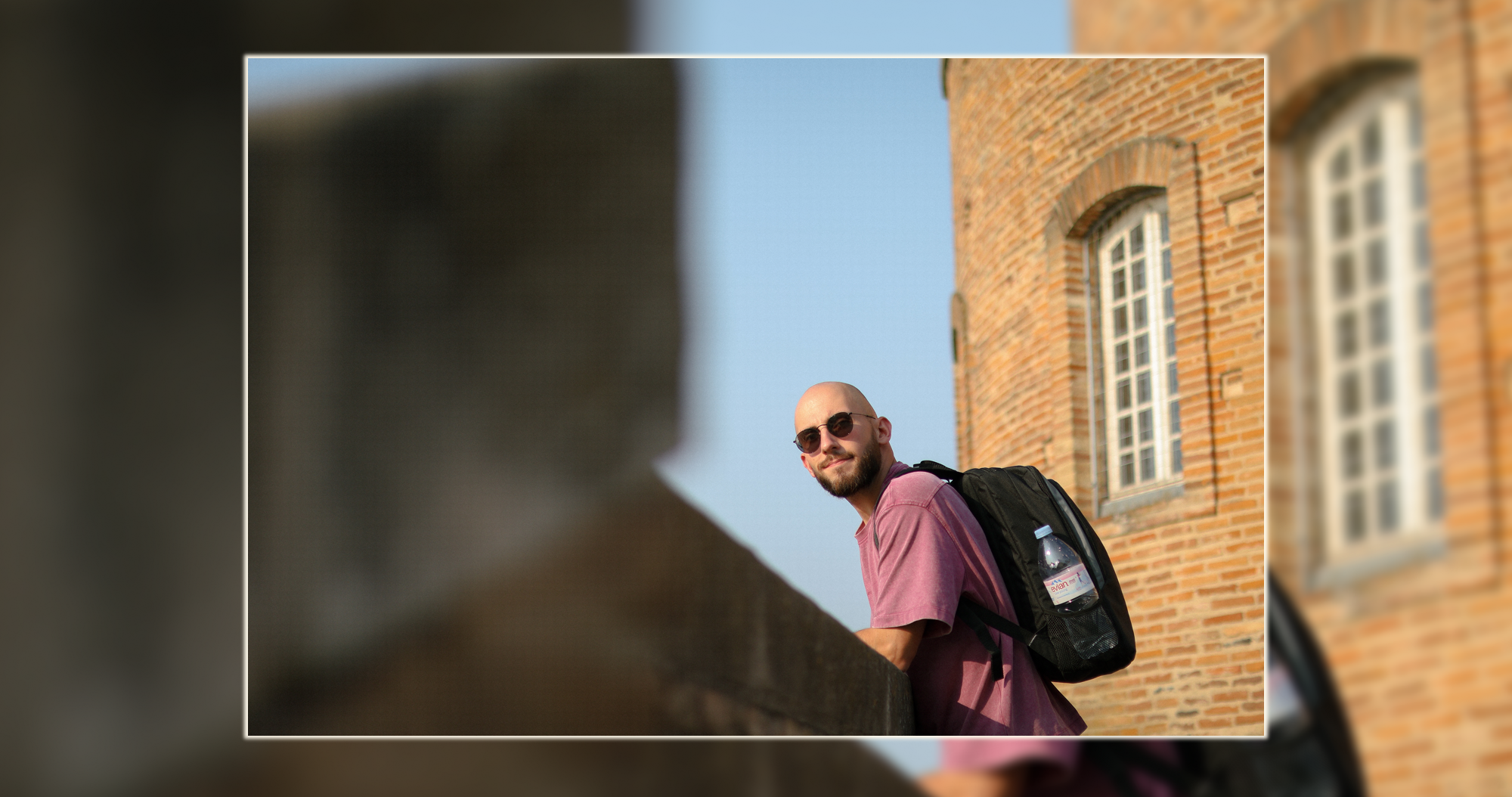 Portrait urbain brique – Lumineo Portrait d’un homme en extérieur appuyé sur un muret avec un bâtiment en briques derrière – photographie portrait urbain par Luminéo