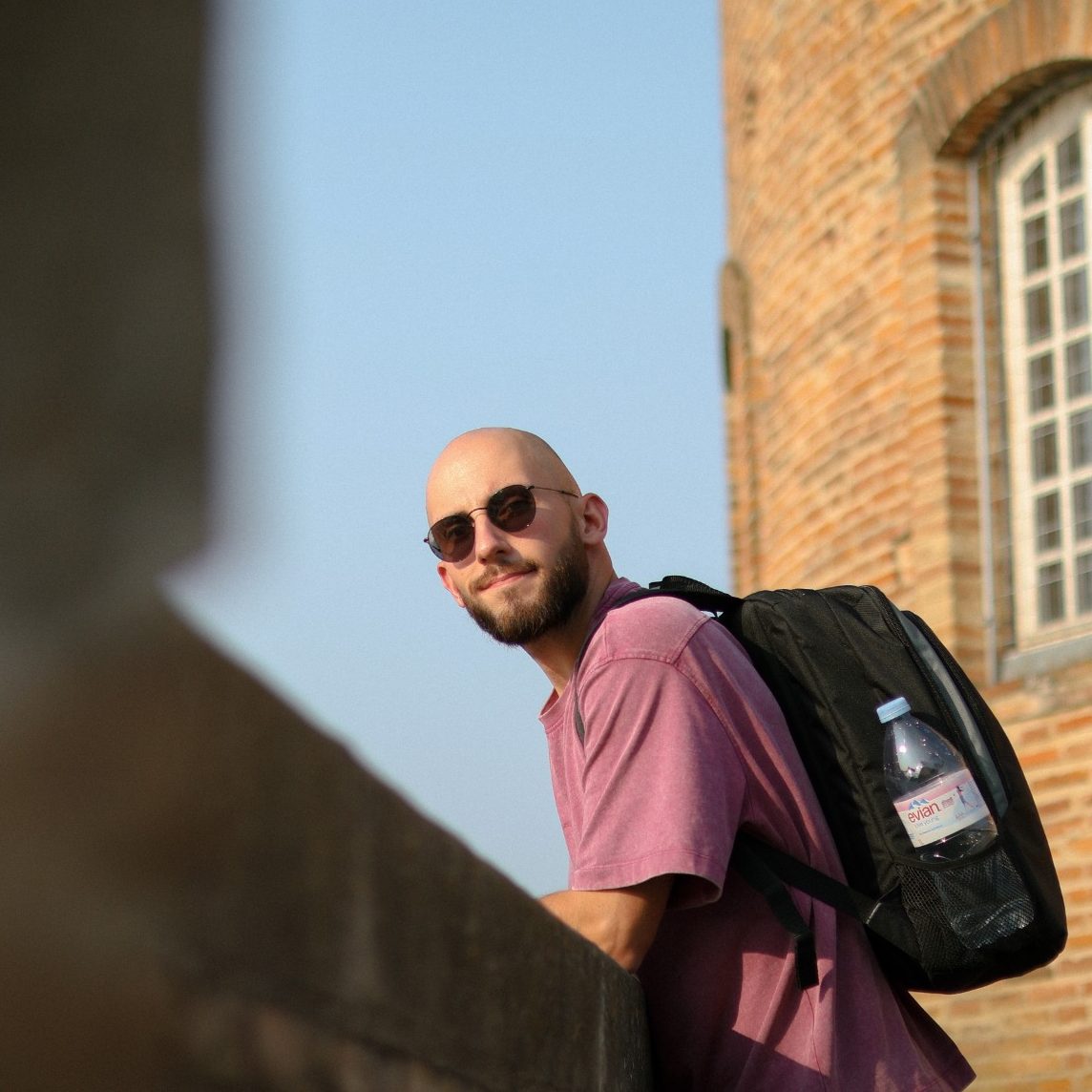 Portrait d’un homme en extérieur appuyé sur un muret avec un bâtiment en briques derrière – photographie portrait urbain par Luminéo