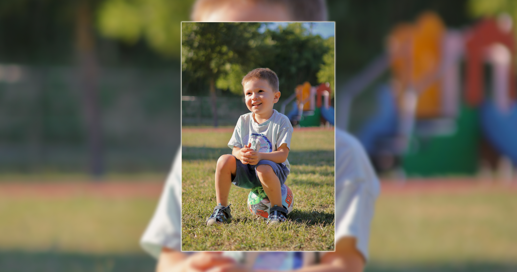 Enfant en extérieur – Luminéo Jeune garçon souriant assis sur un ballon dans un parc, scène ensoleillée – photo d’enfance Luminéo